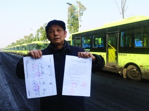 劉明手持多個部門的審批文件，身后就是閑置在路邊的電動公交車